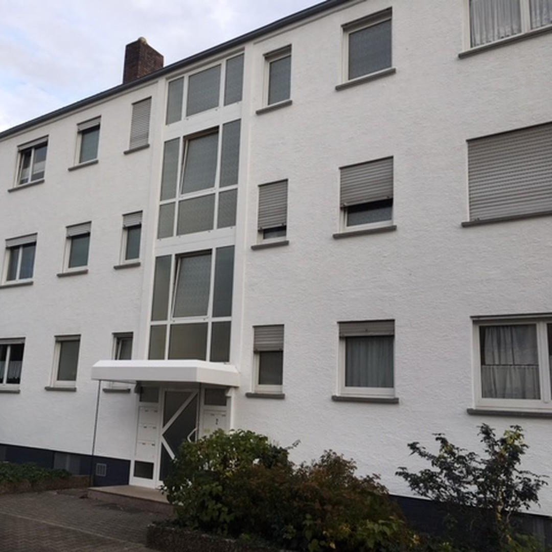Mehrfamilienhaus mit hellem Putz und Treppenhausfenstern, Straßenansicht